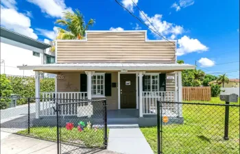 Single-story residence featuring horizontal lap siding, a metal-roofed covered front porch with decorative millwork, grid-pane windows with shutters, and a gated chain-link fence