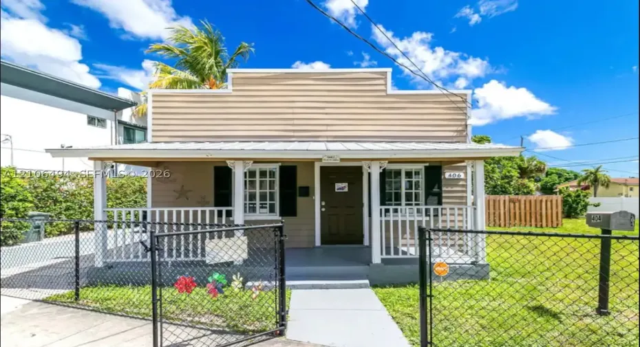 Single-story residence featuring horizontal lap siding, a metal-roofed covered front porch with decorative millwork, grid-pane windows with shutters, and a gated chain-link fence