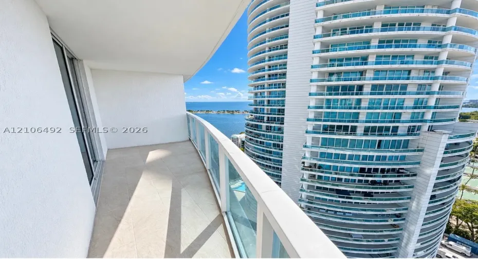 Private balcony featuring neutral tile flooring, glass panel railings, and water scenery