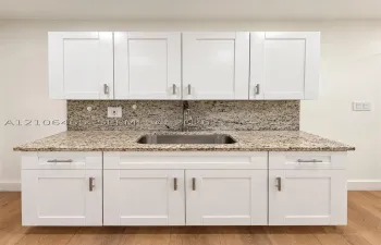Shaker-style white cabinetry featuring brushed nickel pulls, stone countertop, undermount stainless steel sink, matching stone backsplash, and wood-finish flooring