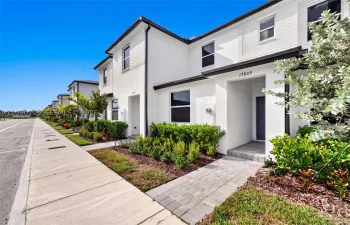 Contemporary two-story exterior featuring white stucco finish, dark-toned trim, a stone paver walkway, and structured shrubbery