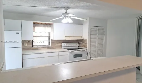 Kitchen featuring white cabinetry, stone-finish backsplash, built-in range, refrigerator, and solid surface breakfast bar