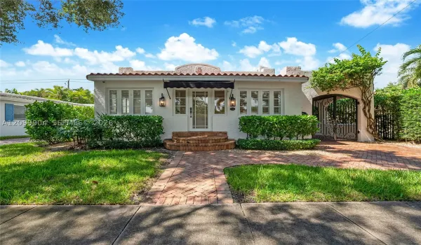 Spanish-style exterior featuring a clay tile roof, stucco facade, arched gate, brick paver walkway, and stone-tread entry steps