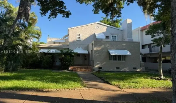 Stucco exterior residence featuring a tiled chimney, decorative geometric window accents, metal window awnings, and a brick-stepped entryway