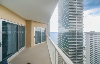 Covered balcony featuring concrete flooring, white metal railing, and multi-panel sliding glass doors