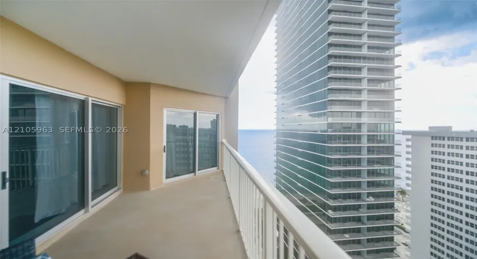 Covered balcony featuring concrete flooring, white metal railing, and multi-panel sliding glass doors