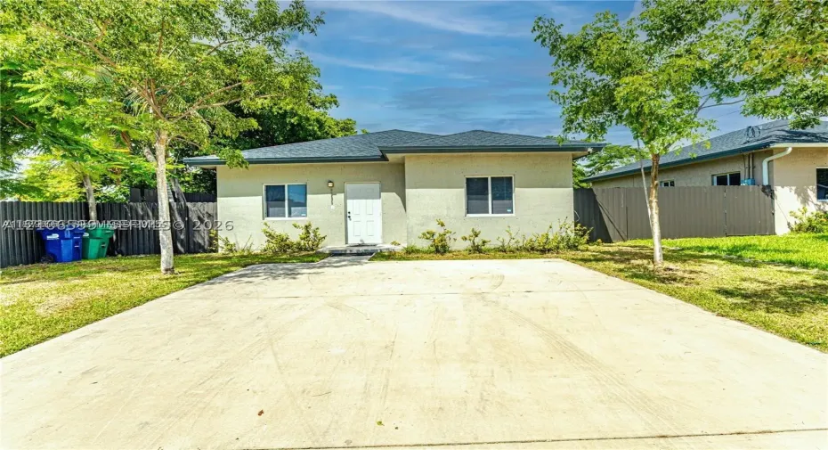 Single-story stucco exterior with a hip roof, concrete driveway, and metal perimeter fencing