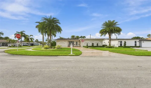 Single-story exterior featuring arched architectural accents, a paved driveway, and mature palm trees within a landscaped yard