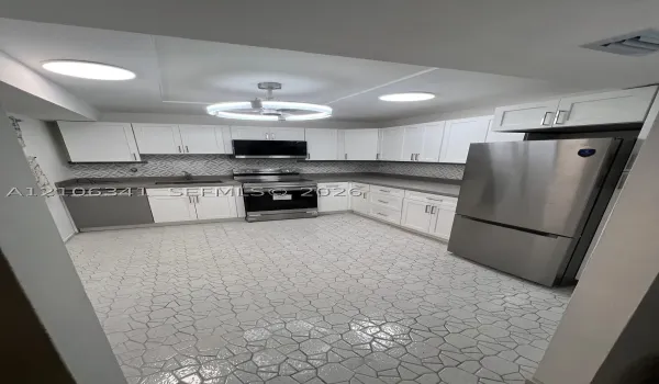 Kitchen featuring white shaker-style cabinetry, stainless steel appliances, patterned tile backsplash, solid-surface countertops, and geometric tile flooring