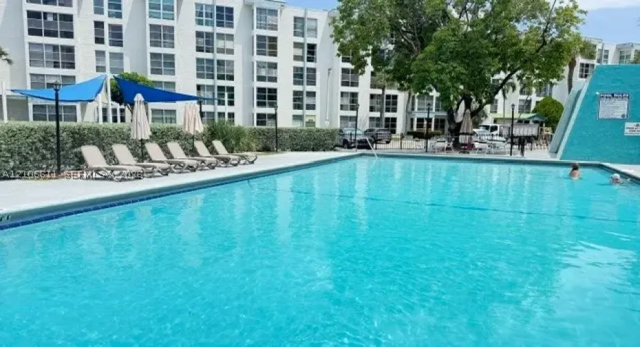 Community swimming pool featuring a concrete deck, tiled perimeter, and blue fabric sun shades
