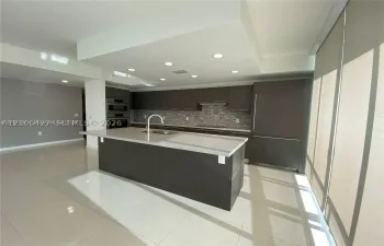 Contemporary kitchen featuring dark cabinetry, a central island with a solid-surface countertop, an integrated refrigerator, recessed ceiling lighting, and a neutral-toned backsplash