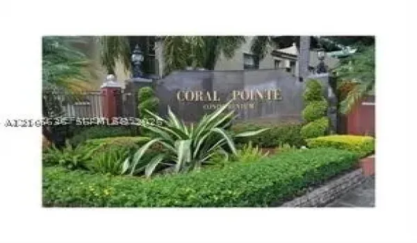 Stone monument signage featuring metallic lettering, complemented by manicured shrubbery, decorative topiary, and palm plantings