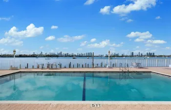 Rectangular swimming pool with paved decking, metal perimeter fencing, and water backdrop