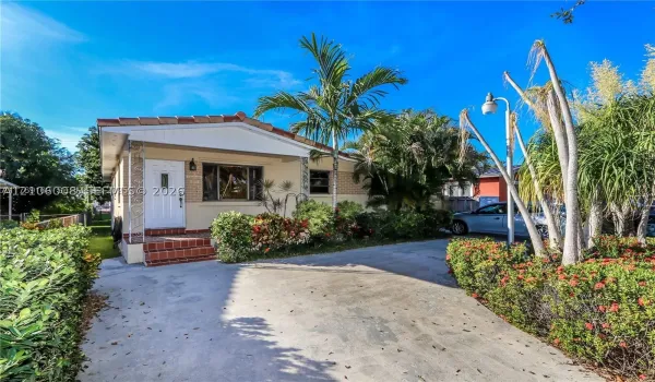 Single-story exterior featuring a concrete driveway, terracotta-toned masonry entrance steps, and manicured landscaping including established palm trees