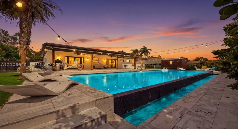 Expansive outdoor area featuring a large swimming pool with an integrated waterfall, a spacious patio with multiple access points to the residence, and mature tropical landscaping