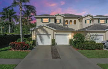 Stucco exterior featuring two garage bays, concrete driveway, arched window detailing, and manicured landscaping