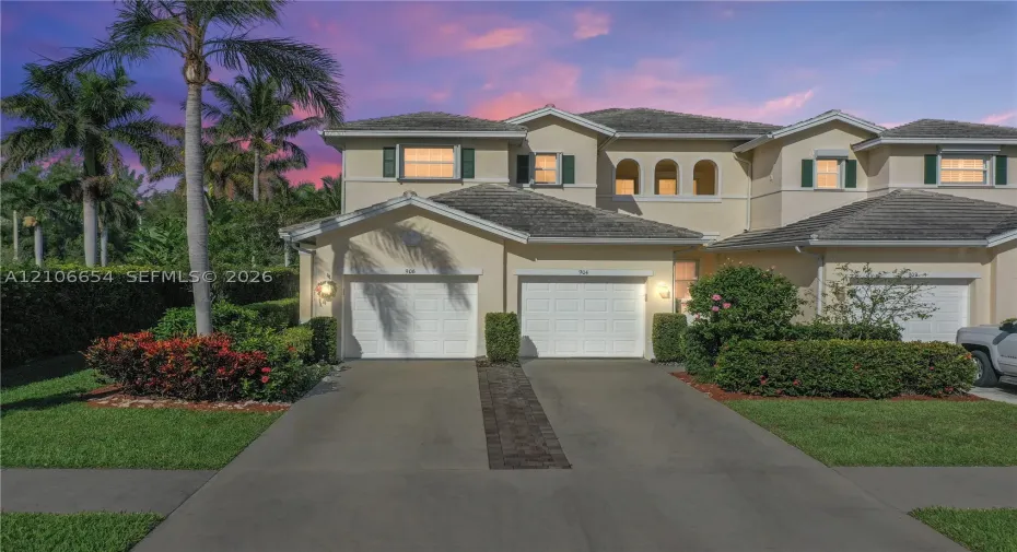 Stucco exterior featuring two garage bays, concrete driveway, arched window detailing, and manicured landscaping