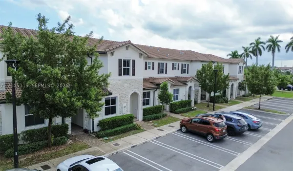 Multi-story townhouse exterior featuring a light-toned stone facade, tiled roofing, decorative shutters, and manicured shrubbery
