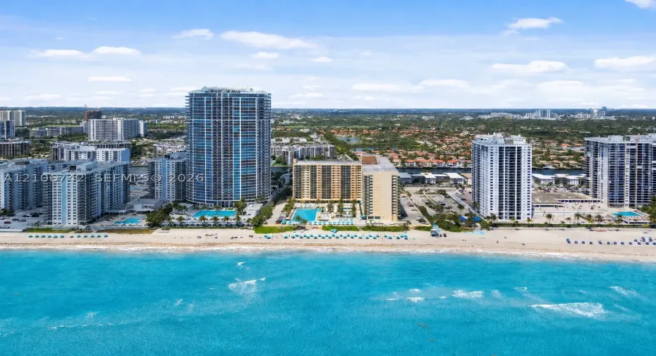 High-rise coastal property featuring direct oceanfront access, private swimming pool, landscaped grounds, and paved parking areas