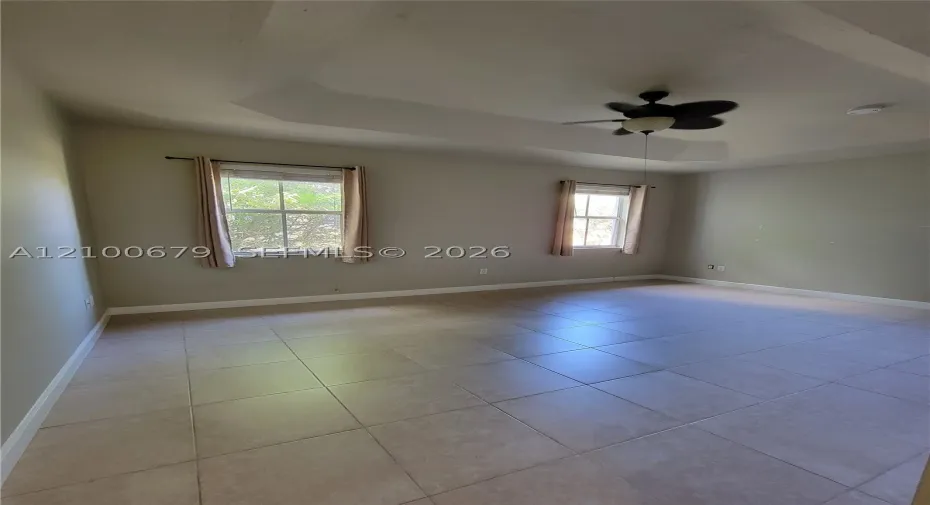 Room featuring a tray ceiling, neutral-toned tile flooring, and a multi-blade ceiling fan