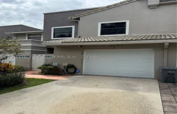 Two-story stucco exterior featuring a concrete tile roof, single-car garage with a sectional door, and an integrated private gated entrance