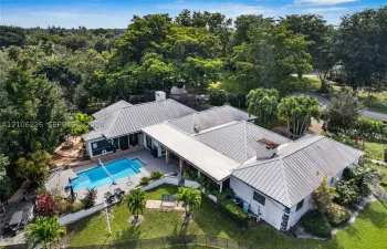 Metal-roofed residence featuring an inground swimming pool, paved patio, expansive lawn, and mature trees