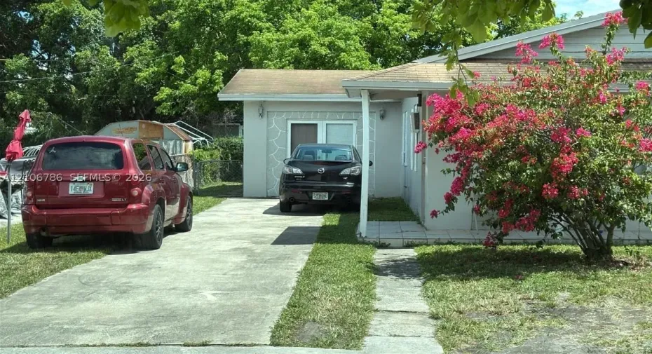 Single-story exterior featuring light-toned masonry, a concrete driveway, a covered front entry, and mature landscaping