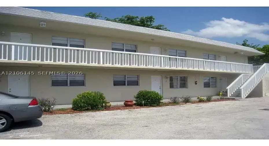 Two-story exterior featuring a white picket-style balcony railing, concrete staircase, neutral stucco facade, and multi-pane windows