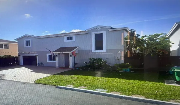 Two-story exterior featuring a light-toned stucco facade, paver driveway, integrated garage, and a covered entryway