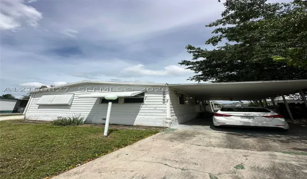 Exterior featuring white horizontal siding, an attached metal carport, window awnings, and an outdoor post-mounted light fixture