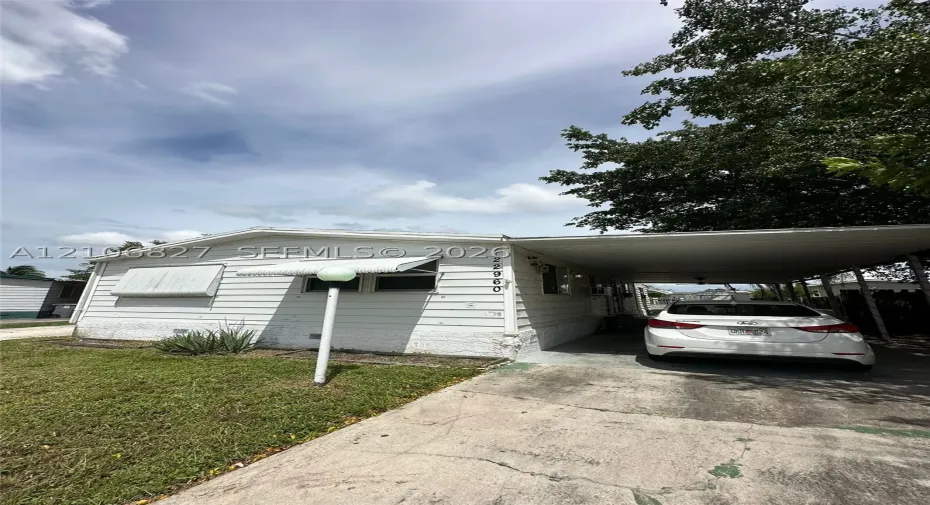 Exterior featuring white horizontal siding, an attached metal carport, window awnings, and an outdoor post-mounted light fixture