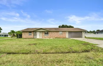 Single-story ranch exterior featuring a brick facade, shingle roof, attached two-car garage, and a concrete driveway
