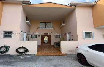 Stucco exterior featuring a covered recessed entryway, decorative front door with oval glass insert, tiled porch, and upper-level exterior balcony with metal railing