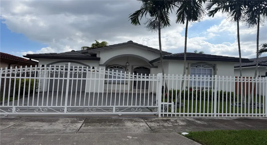 Single-story residence featuring a gated entry, arched front porch, tile roof, arched windows, and mature palm trees