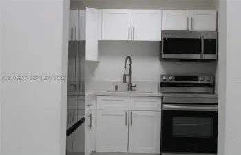 Kitchenette featuring white Shaker-style cabinetry, stainless steel appliances, a stone-composite countertop, and a gooseneck faucet