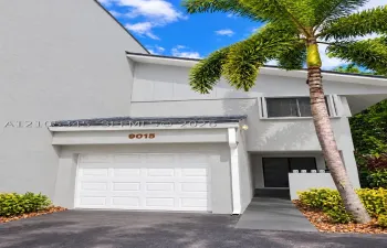Modern exterior featuring a light gray facade, single-car garage, recessed entryway, and a concrete walkway bordered by mature landscaping