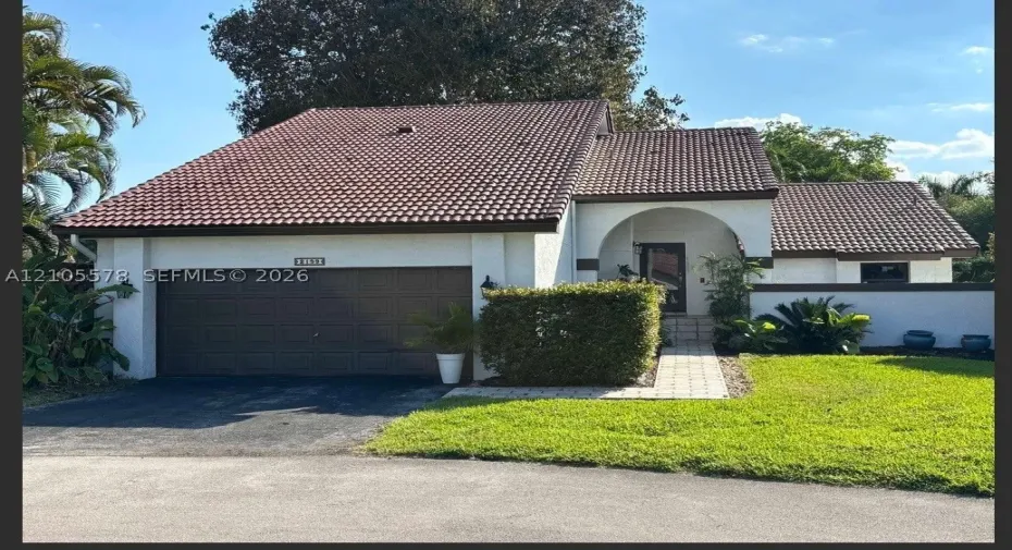Exterior featuring a concrete tile roof, stucco finish, arched entryway, and attached two-car garage