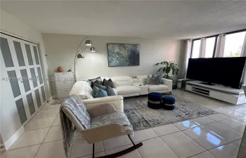 Open-concept room featuring light-toned tile flooring, floor-to-ceiling windows with window treatments, and closet doors with glass panel inserts