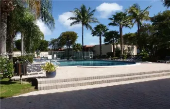 In-ground swimming pool featuring concrete paver decking, multi-level stairs, perimeter fencing, and surrounding palm trees