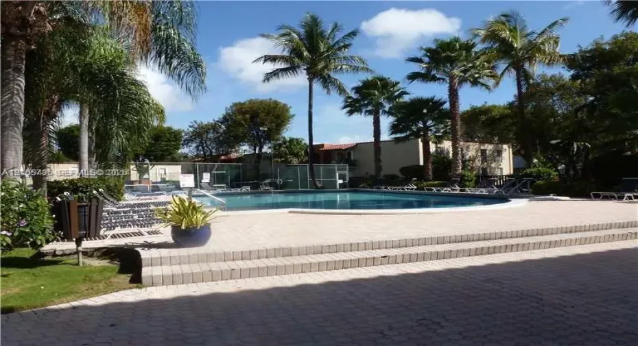 In-ground swimming pool featuring concrete paver decking, multi-level stairs, perimeter fencing, and surrounding palm trees