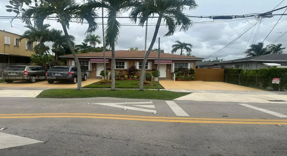 Single-story exterior featuring a hip roof, dual entryways with retractable fabric awnings, and an expansive paved driveway