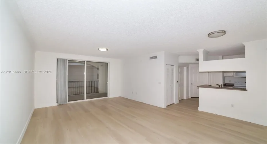 Wood-finish flooring, sliding glass door to a balcony with metal railings, built-in breakfast bar, white cabinetry, and recessed lighting