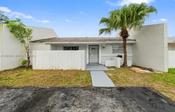 Single-story residence featuring a private walled courtyard, concrete walkway, metal security door, and a prominent palm tree