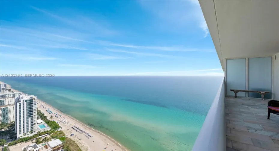 Covered balcony featuring stone tile flooring, frosted glass privacy panel, and expansive ocean scenery