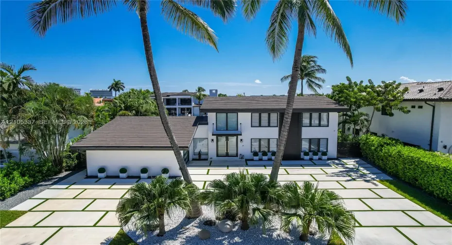 Two-story residence featuring a crisp white exterior, dark-toned roof, paved driveway with grass grid detail, multi-pane windows, and a central balcony