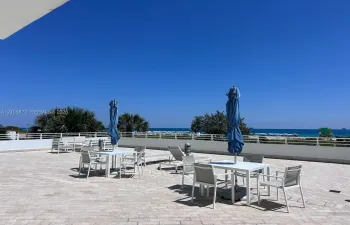 Expansive stone-paved terrace featuring a white metal perimeter railing and coastal horizon