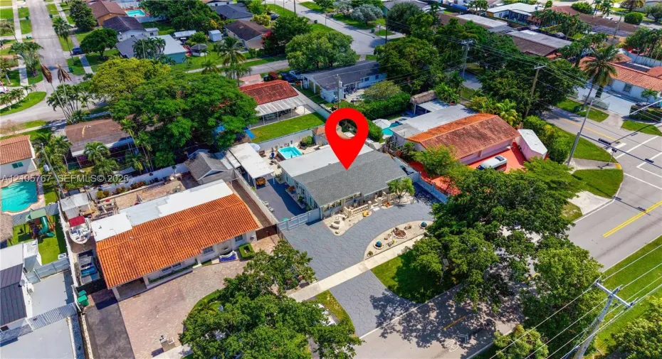 Aerial perspective of a property featuring a pitched shingle roof, paved driveway, carport, and enclosed swimming pool