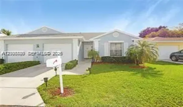 Single-story exterior featuring light-toned siding, dual garage doors, decorative gable accents, and a manicured lawn with mature landscaping