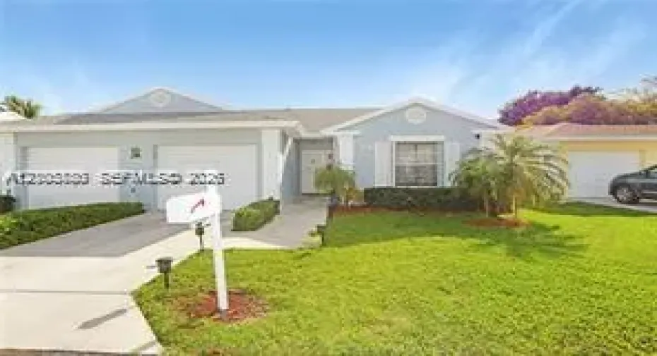 Single-story exterior featuring light-toned siding, dual garage doors, decorative gable accents, and a manicured lawn with mature landscaping