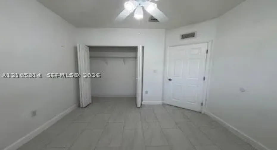 Interior room featuring light-toned tile flooring, a dual-door closet, a six-panel door, and a ceiling fan with integrated lighting